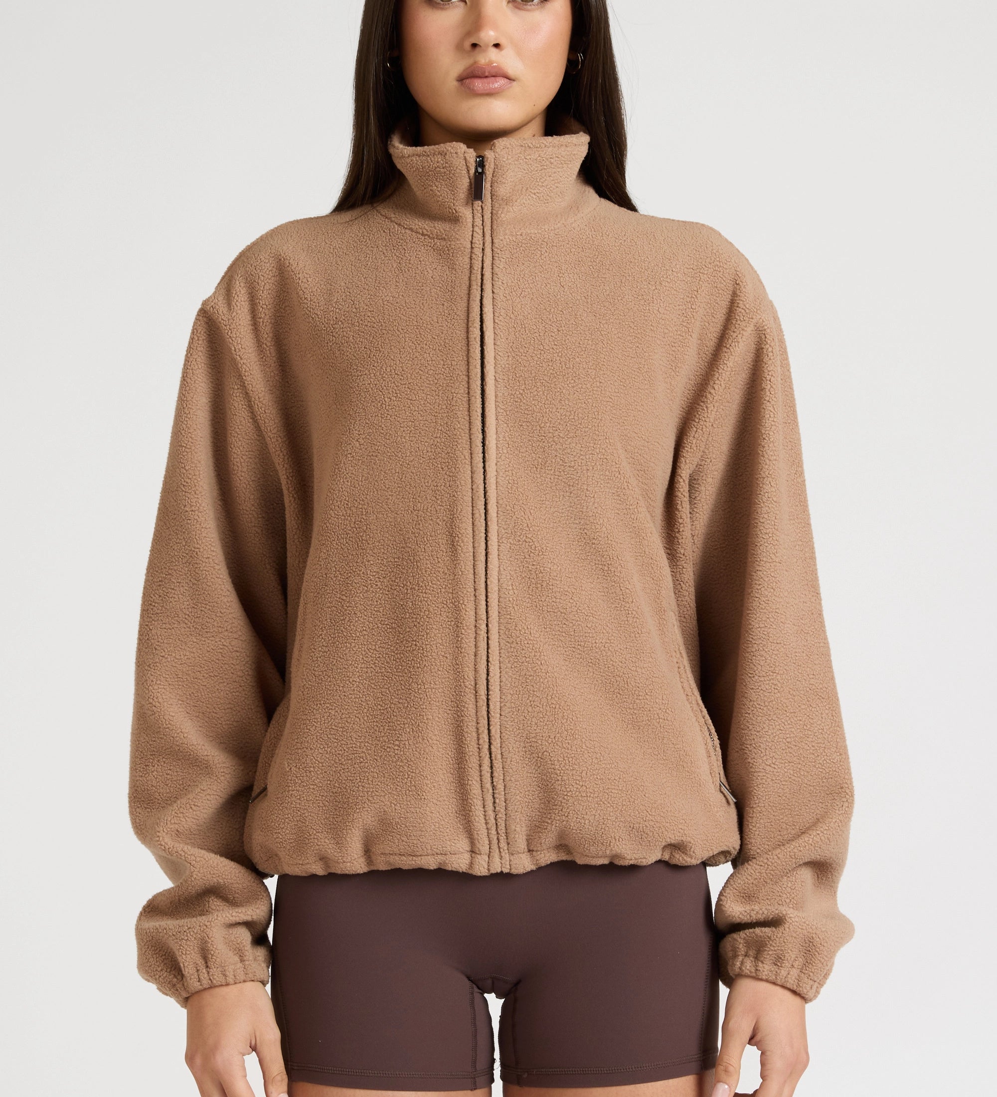 Woman wearing a brown fleece jacket and shorts on a white background